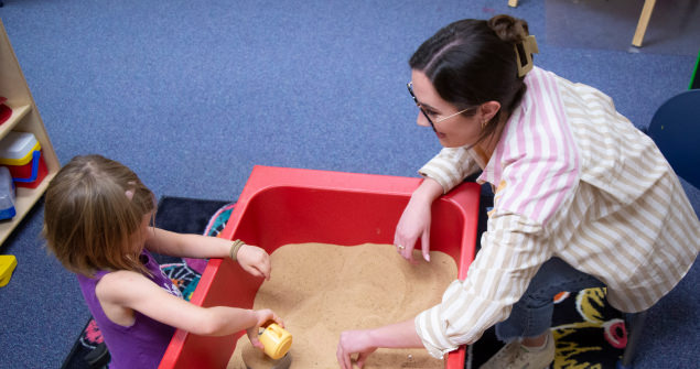 A TCU student playing in a small sandbox with a young child